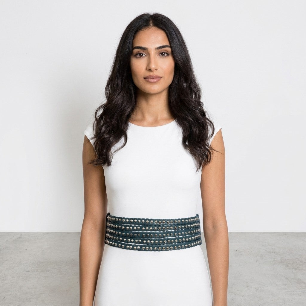 Woman in a white dress with a studded belt, standing against a plain background.