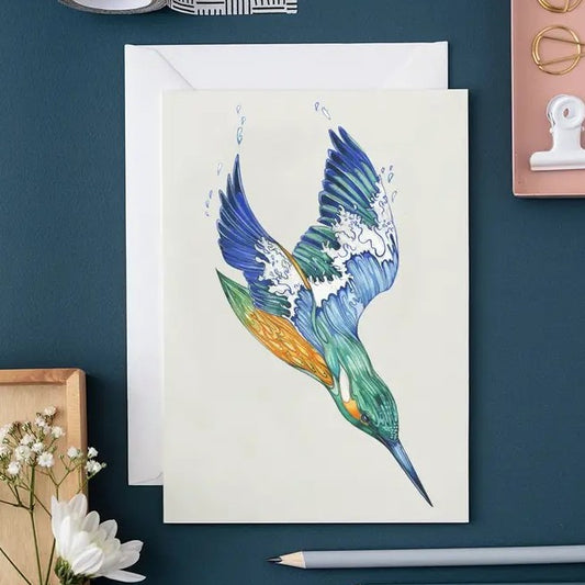 Illustrated bird diving on a card beside a pencil and flowers.