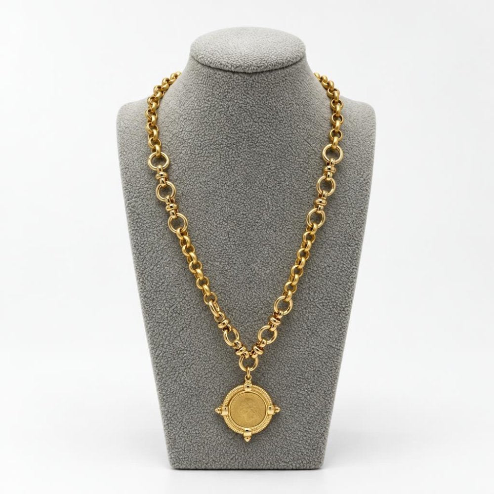 Gold chain necklace with an ornate round medallion displayed on a gray jewelry stand.