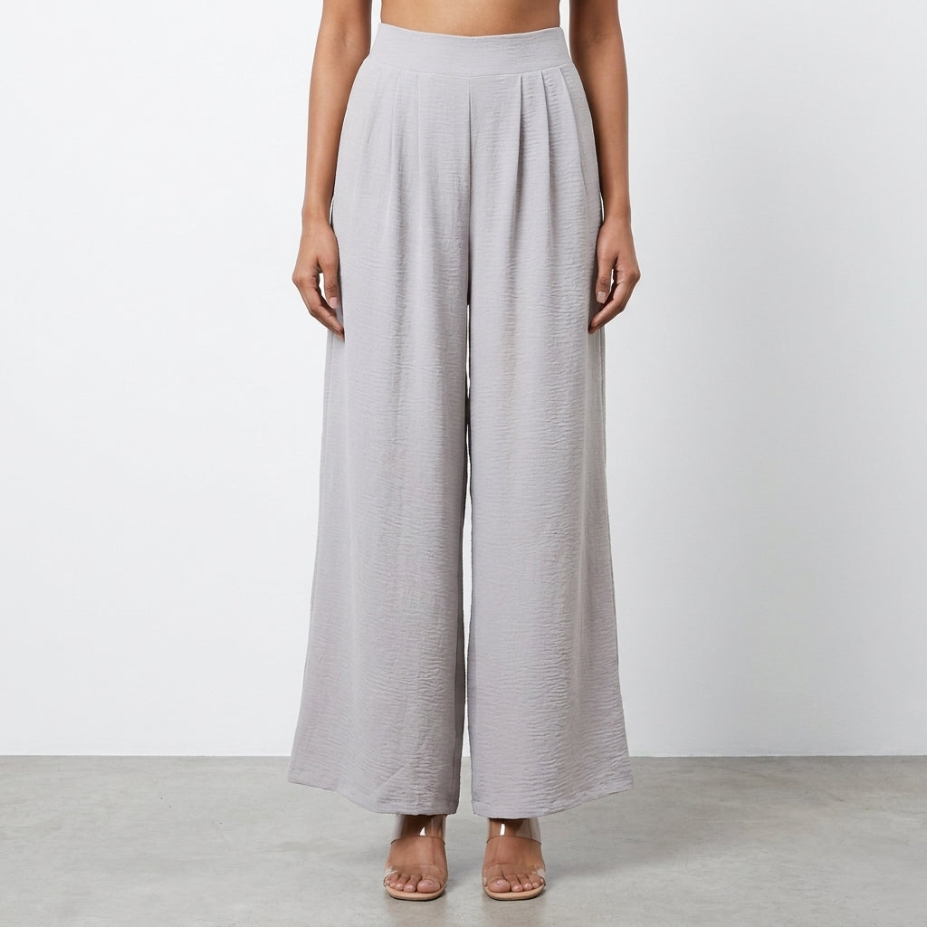 Woman modeling loose gray pants, standing on a neutral background.
