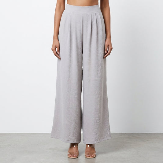 Woman modeling loose gray pants, standing on a neutral background.