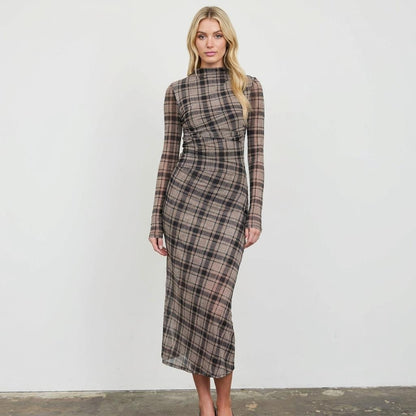 Woman in a long plaid dress poses against a white background.