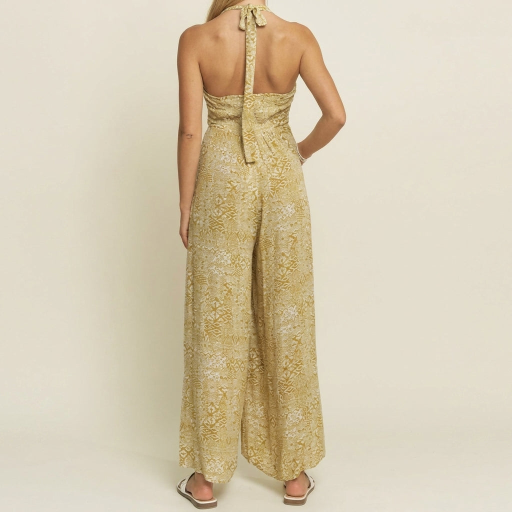 Woman in a backless yellow jumpsuit, facing away, on a plain background.