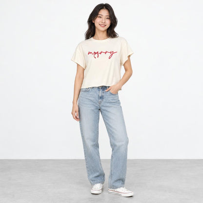 A smiling woman models a cream graphic T-shirt, light-wash jeans, and white sneakers.