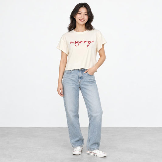 A smiling woman models a cream graphic T-shirt, light-wash jeans, and white sneakers.