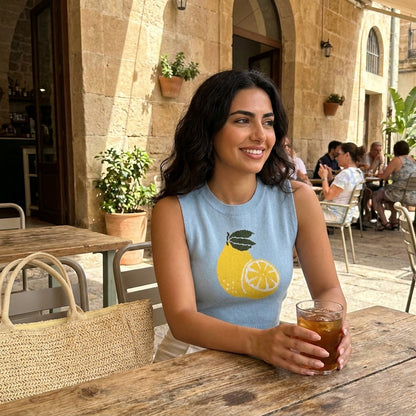 Woman enjoying a drink at an outdoor café, wearing a lemon-themed top.