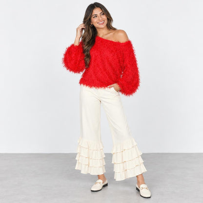A smiling woman models a bright red off-shoulder sweater and cream ruffled pants.