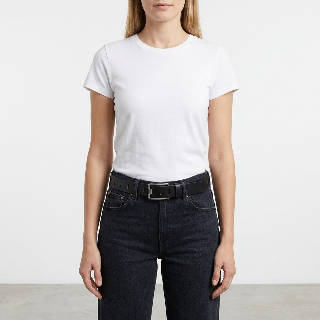 Woman in a white t-shirt and black jeans with a belt, standing indoors.