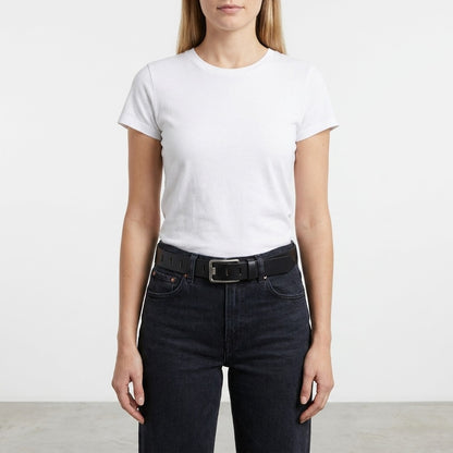 Woman in a white t-shirt and black jeans with a belt, standing indoors.