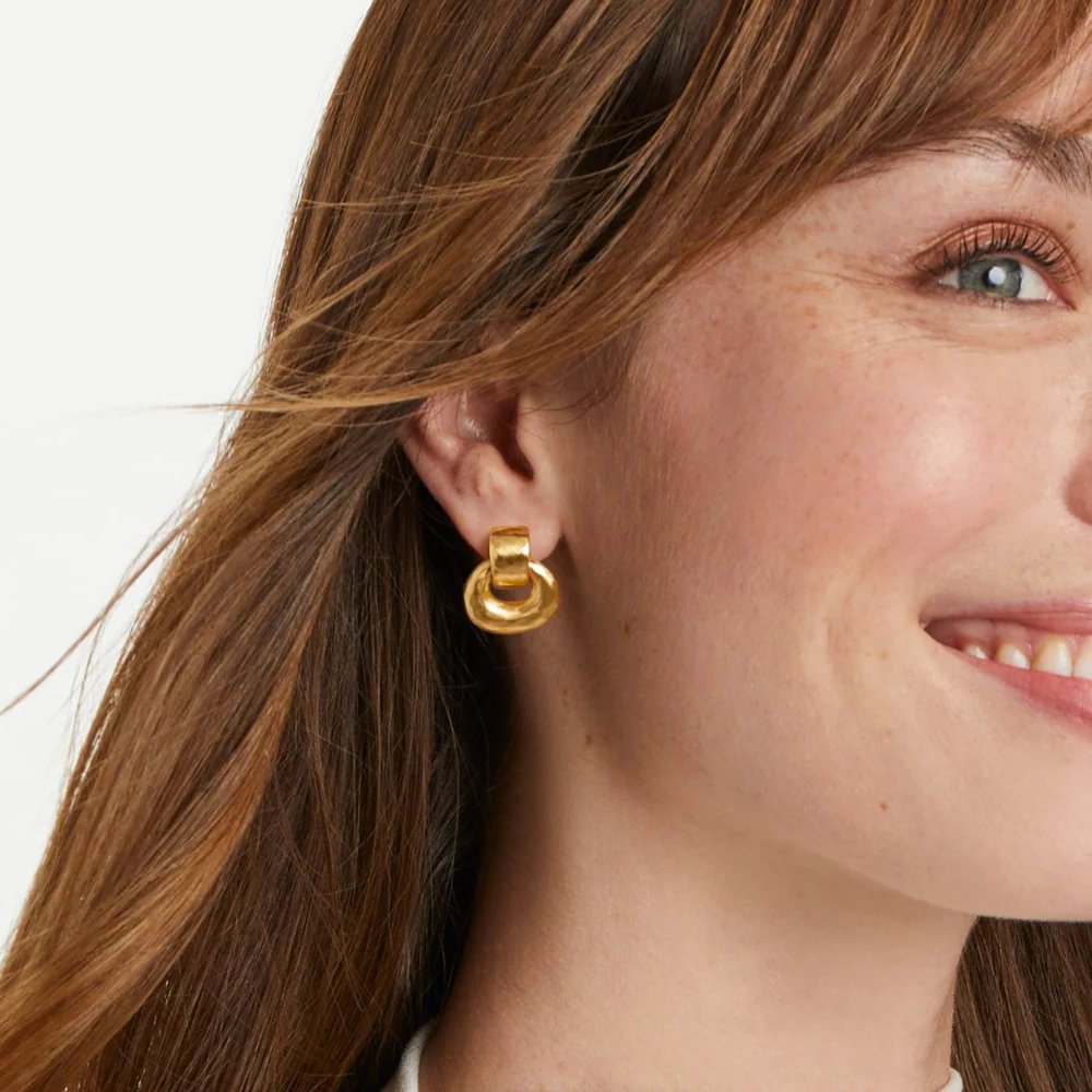 Close-up of a smiling woman wearing a gold statement earring.