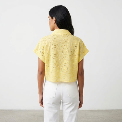Woman in yellow eyelet top and white pants, standing with back to camera.