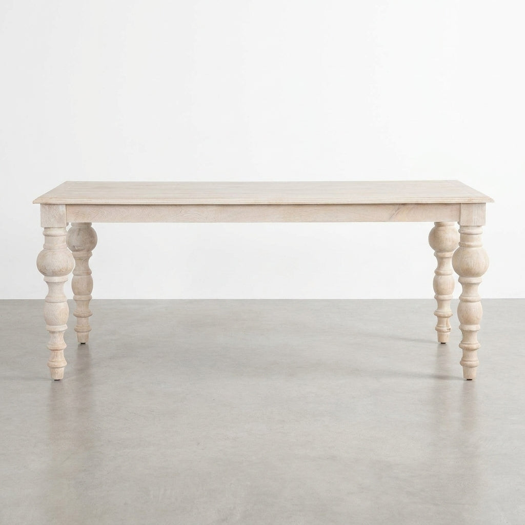 Light wood table with ornate, turned legs on a concrete floor.