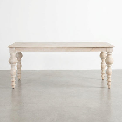 Light wood table with ornate, turned legs on a concrete floor.
