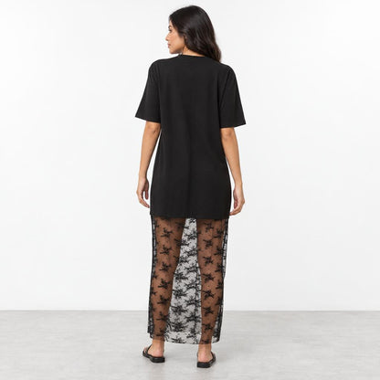 A woman models a black oversized T-shirt dress with a sheer floral lace skirt.