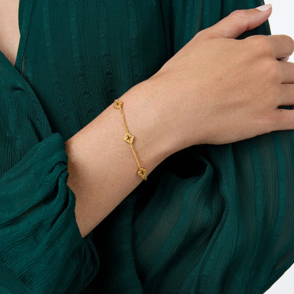 A hand wearing a delicate gold charm bracelet rests against a dark green dress.