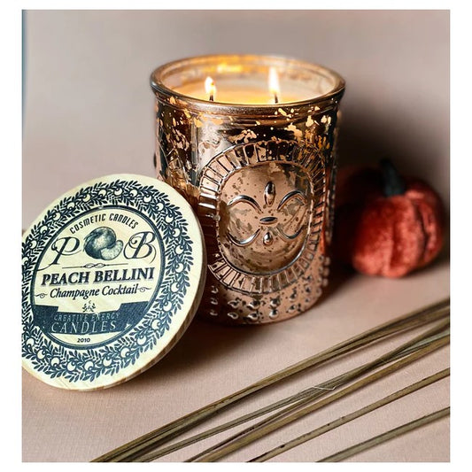 Candle in a decorative glass jar with a small pumpkin and wooden sticks nearby.