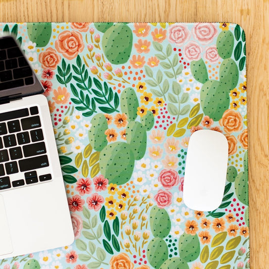 Laptop and mouse on a colorful floral and cactus-patterned desk mat.
