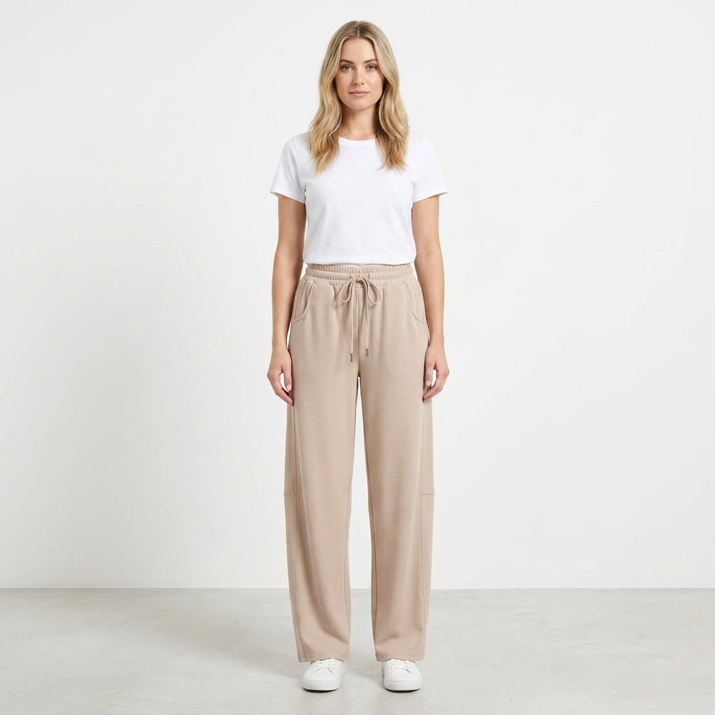 Woman in white t-shirt and beige pants stands against white background.