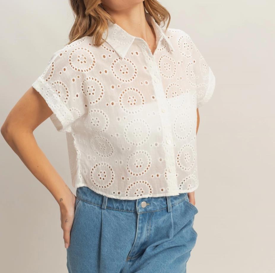 Person in eyelet white shirt and blue jeans against a plain background.