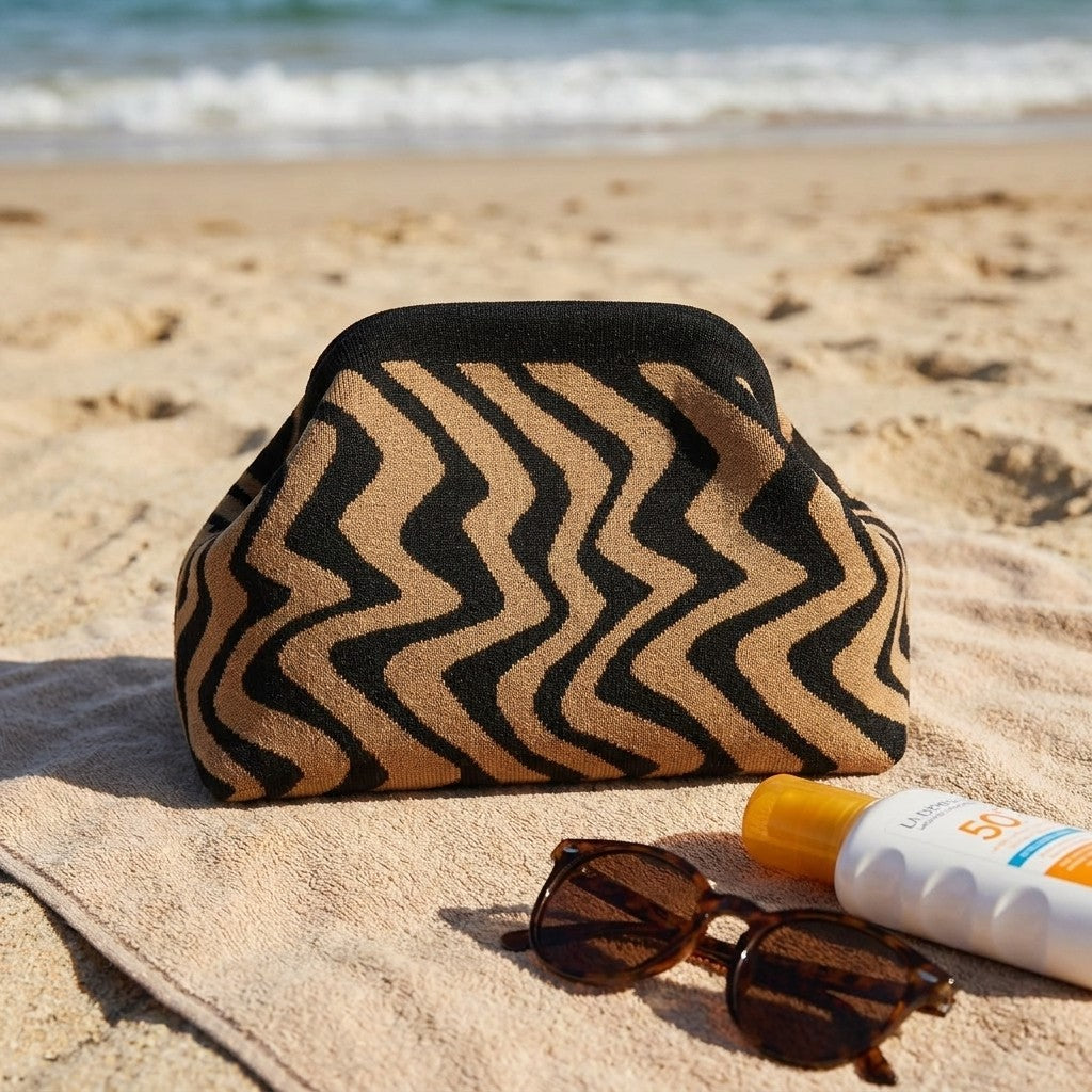 Beach essentials: patterned bag, sunglasses, and sunscreen on a towel by the sea.