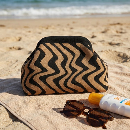 Beach essentials: patterned bag, sunglasses, and sunscreen on a towel by the sea.
