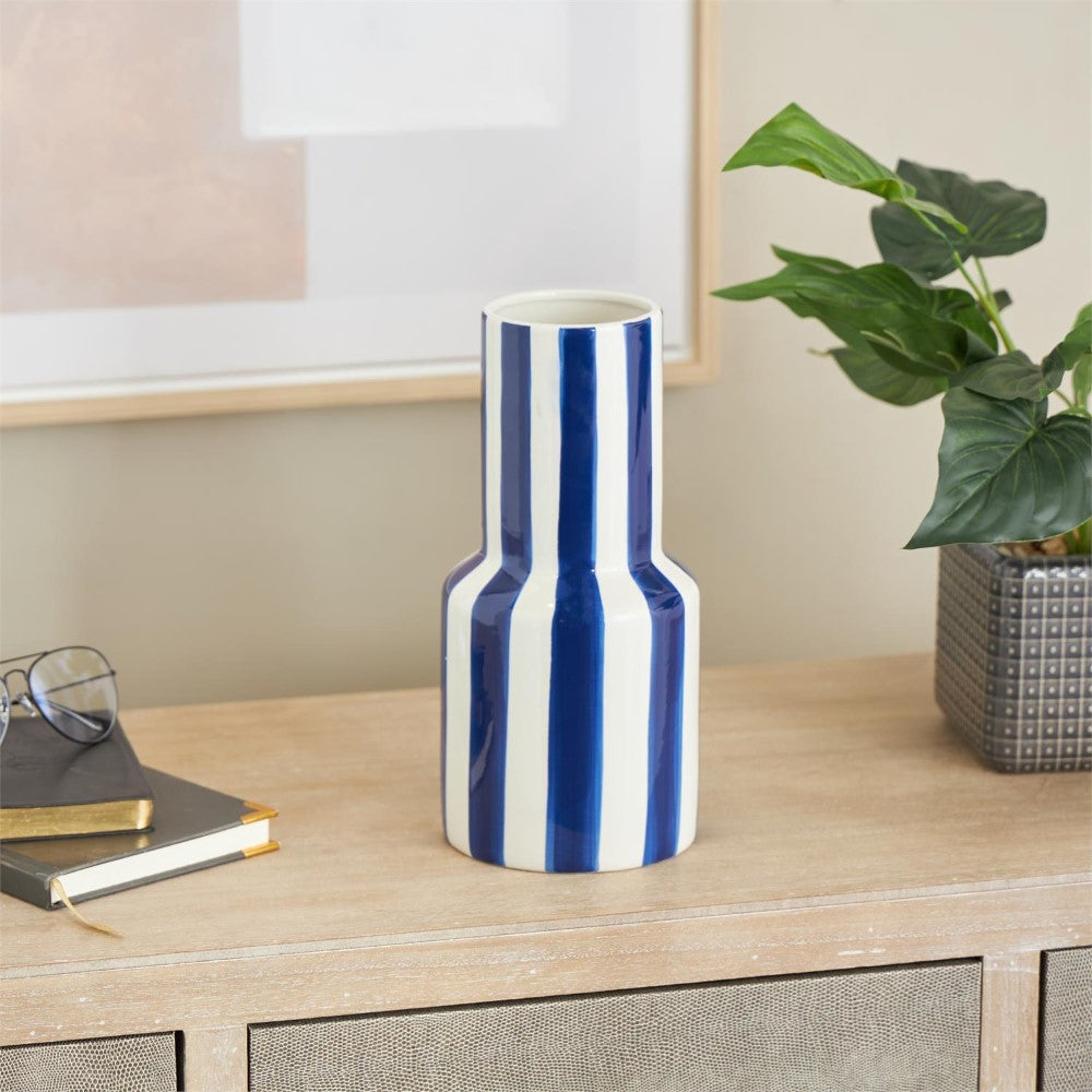 Striped vase on a wooden table with books, glasses, and potted plant.