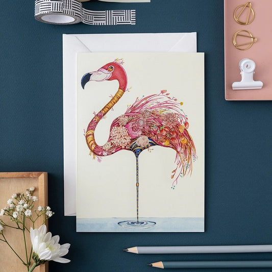 Illustrated flamingo card with stationery on a dark blue surface.
