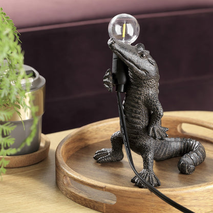 Alligator lamp holding a bulb on a wooden tray.