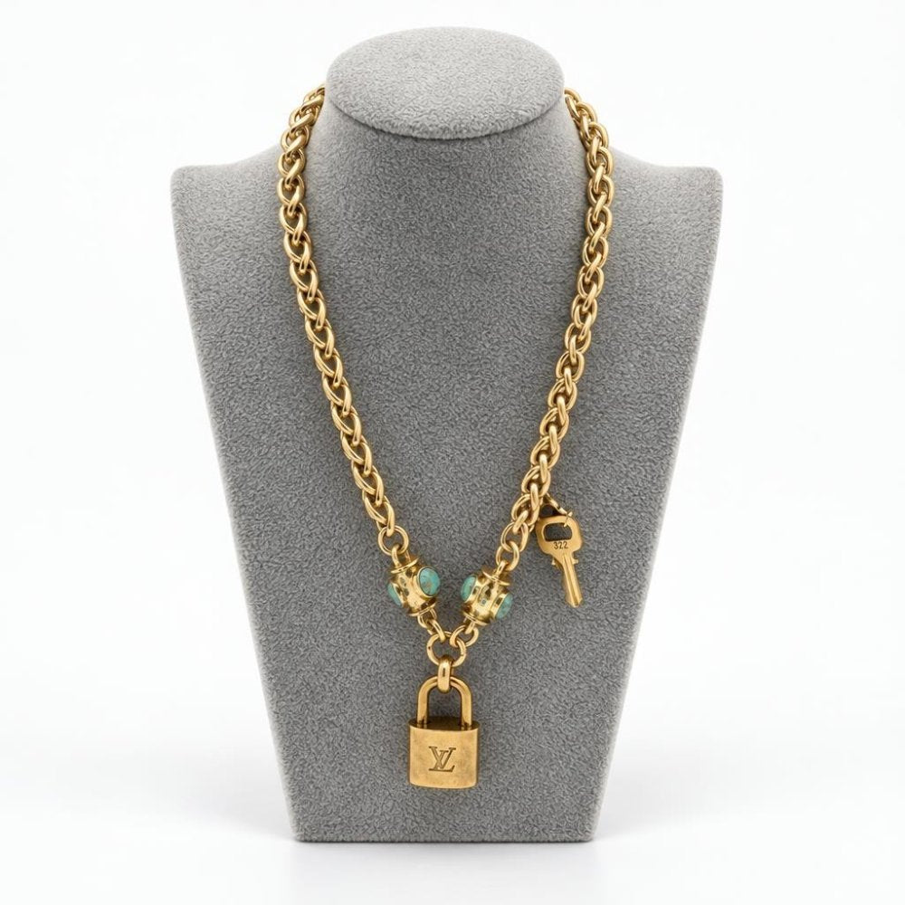 Gold chain necklace with a padlock pendant and key, displayed on a gray jewelry bust.