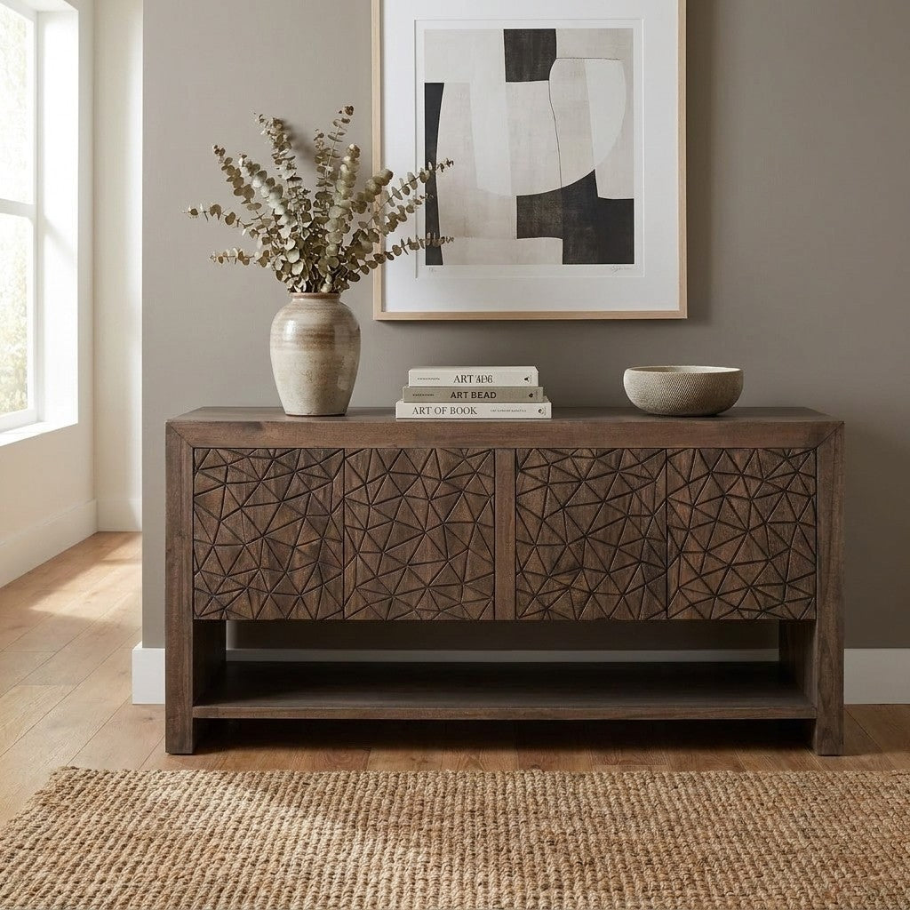 A carved wooden sideboard topped with books, a vase, and a bowl beneath abstract art.