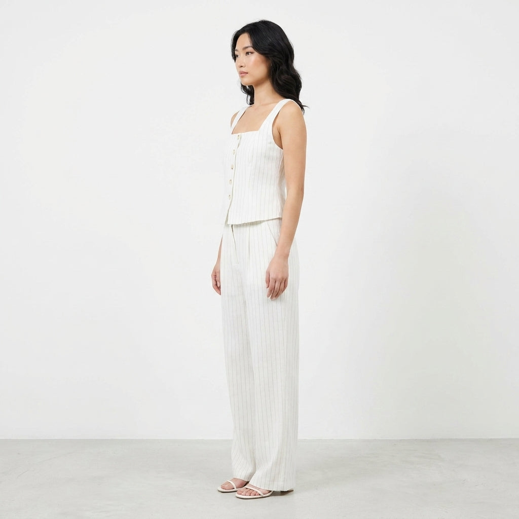 Woman in striped white outfit stands against a plain backdrop.