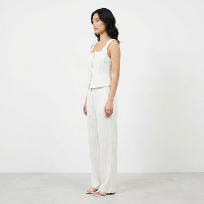 Woman in striped white outfit stands against a plain backdrop.