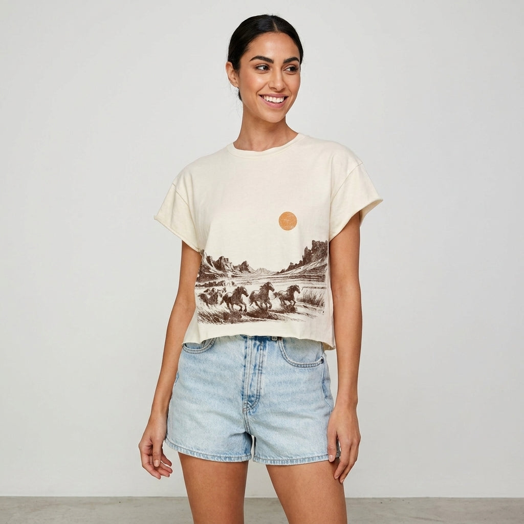 Smiling woman in a desert-themed shirt and denim shorts.