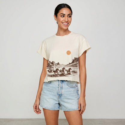 Smiling woman in a desert-themed shirt and denim shorts.