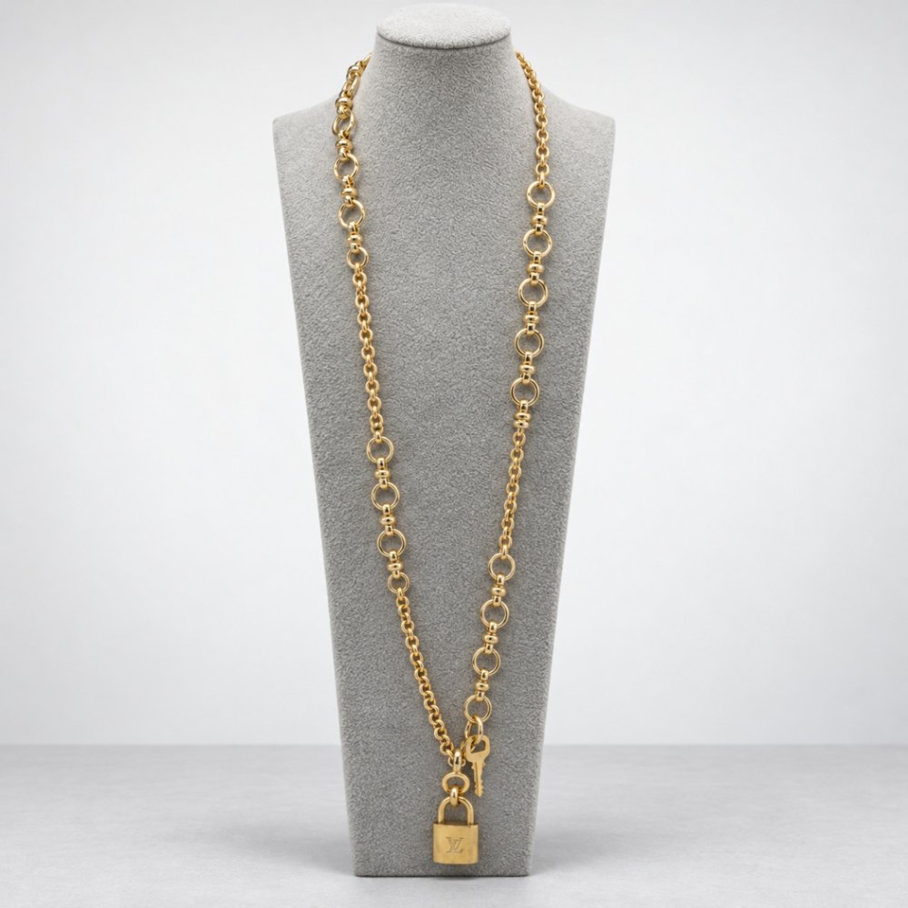 A long gold chain necklace with circular links and a padlock charm displayed on a gray bust.