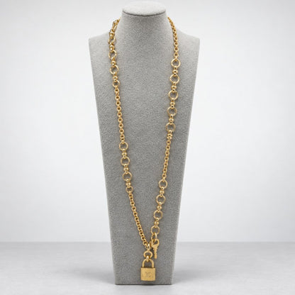 A long gold chain necklace with circular links and a padlock charm displayed on a gray bust.