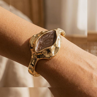 Gold bracelet with a unique, artistic design worn on a wrist.