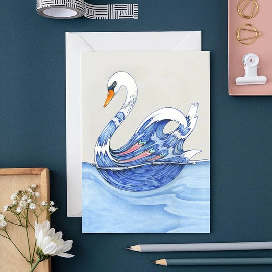 Watercolor swan card on a blue desk with flowers and stationery.