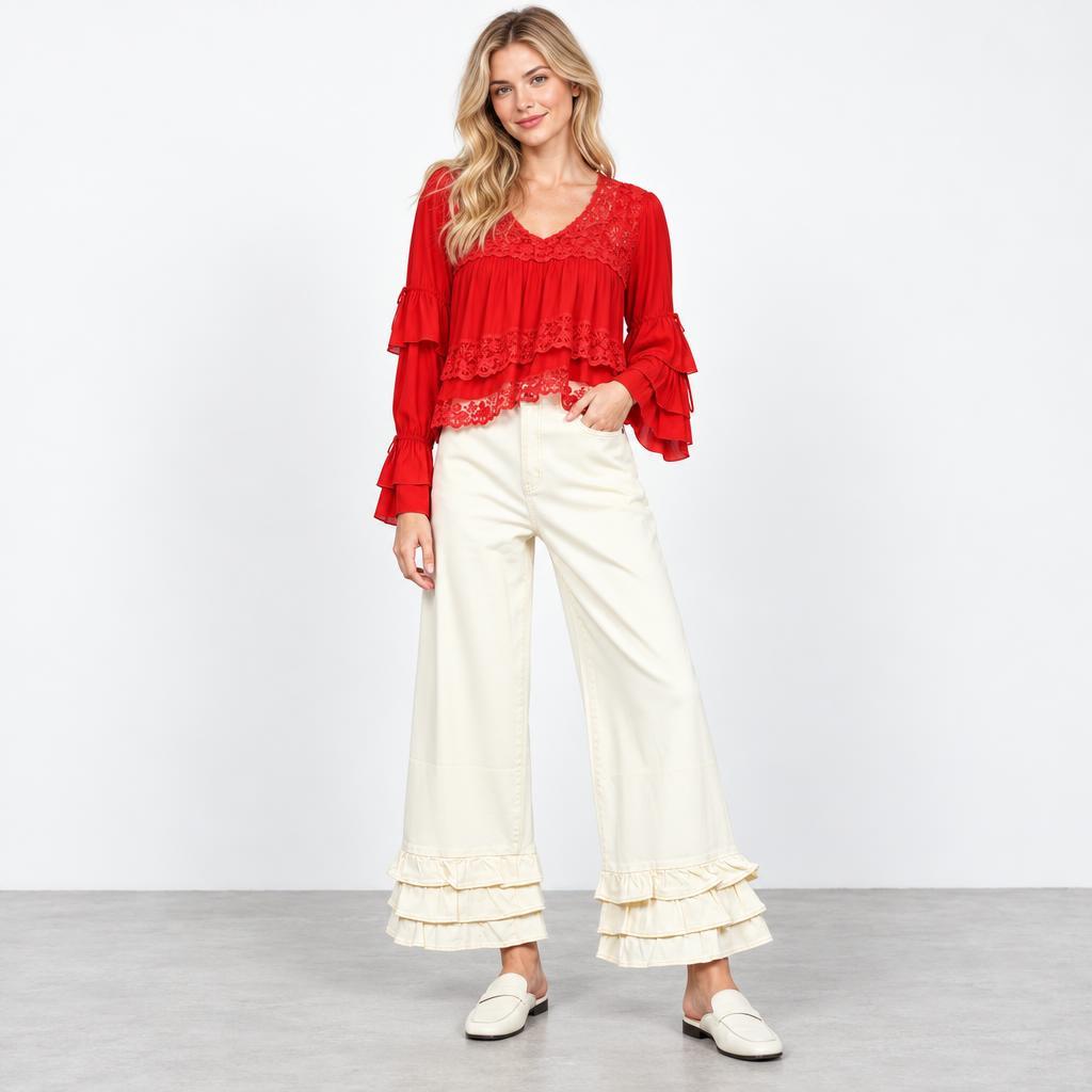 Model wears a red lace-trimmed blouse with ruffled sleeves, cream wide-leg pants, and white loafers.