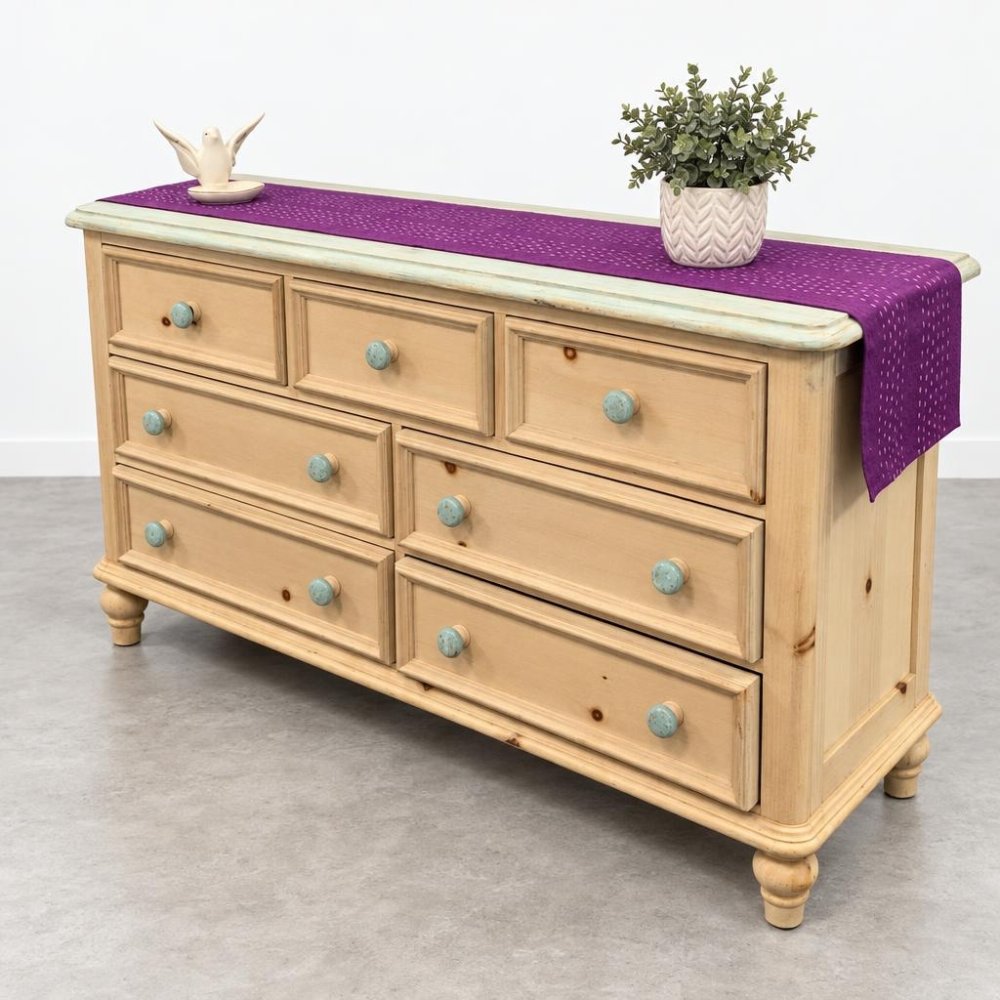 A light wood dresser with turquoise knobs, topped with a purple runner and potted plant.