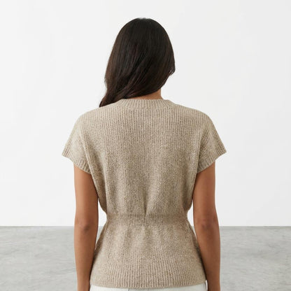 Person in a beige knit top, facing away in a minimalistic setting.