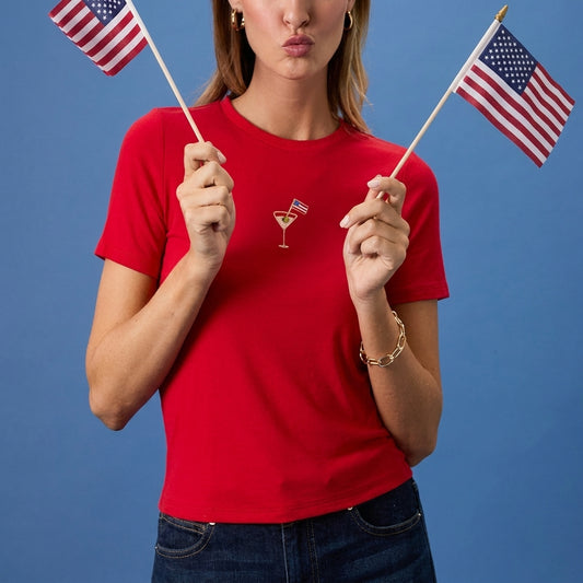 Woman in red tee holding two American flags against a blue background.