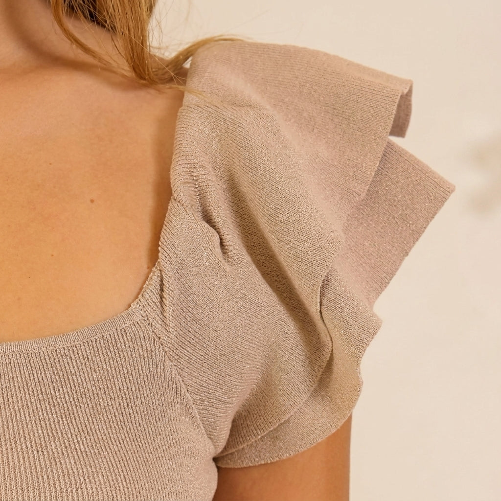 Close-up of a beige knit top with ruffled sleeves.