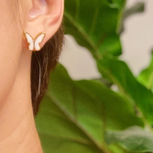 Butterfly earring on an ear with a green leafy background.