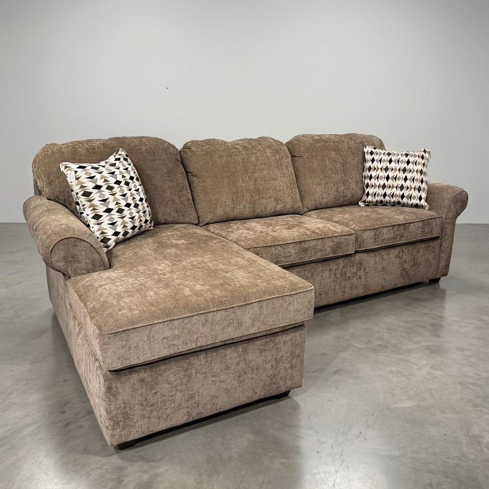Brown sectional sofa with two patterned pillows on a polished concrete floor.