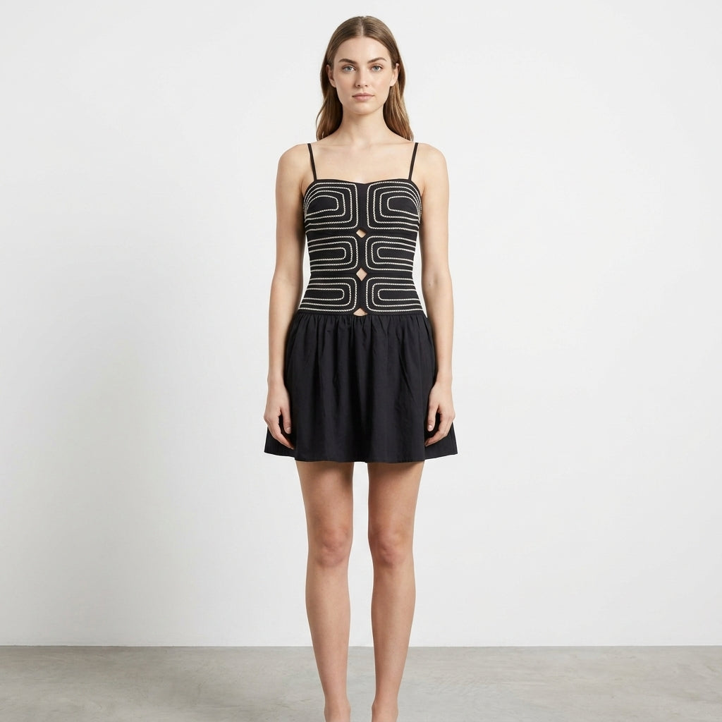 Woman in geometric black mini dress, neutral background.