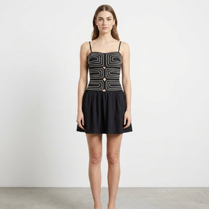Woman in geometric black mini dress, neutral background.
