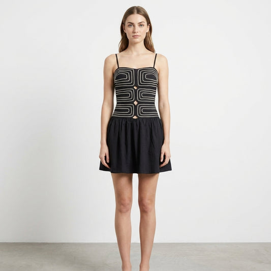 Woman in geometric black mini dress, neutral background.