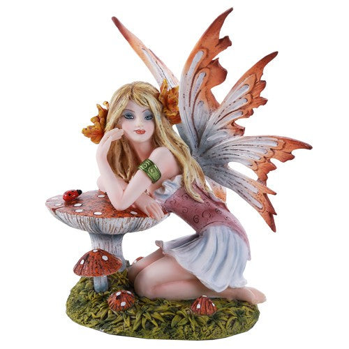 Fairy figurine with orange wings kneeling beside mushrooms.