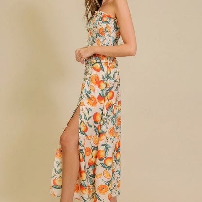 Woman in orange-print dress with slit, neutral background.